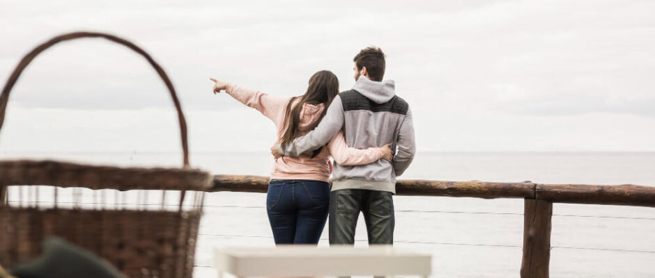 Couple hugging and pointing at the sea during a picnic.