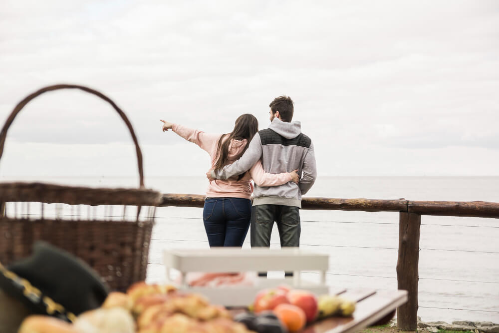 Couple hugging and pointing at the sea during a picnic.