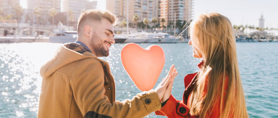 Romantic couple with heart balloon sitting by the harbor.