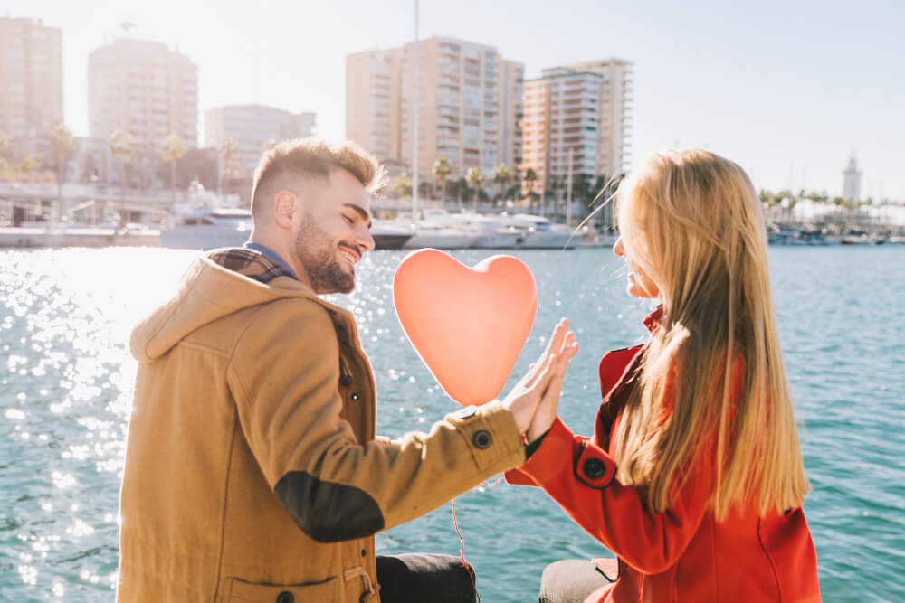 Romantic couple with heart balloon sitting by the harbor.
