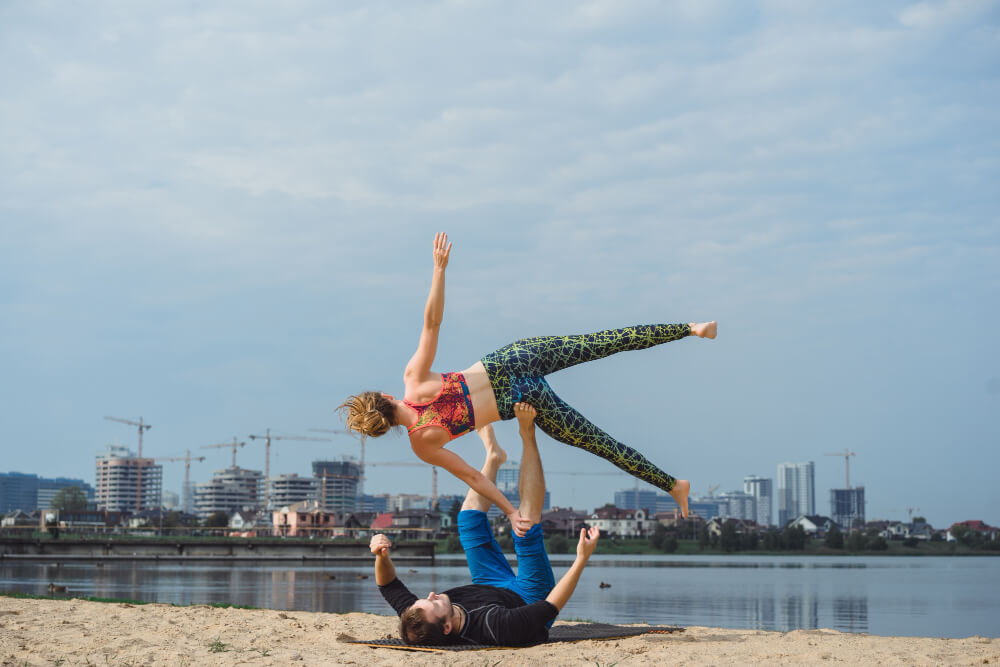 A man and woman performing acroyoga on a beach.