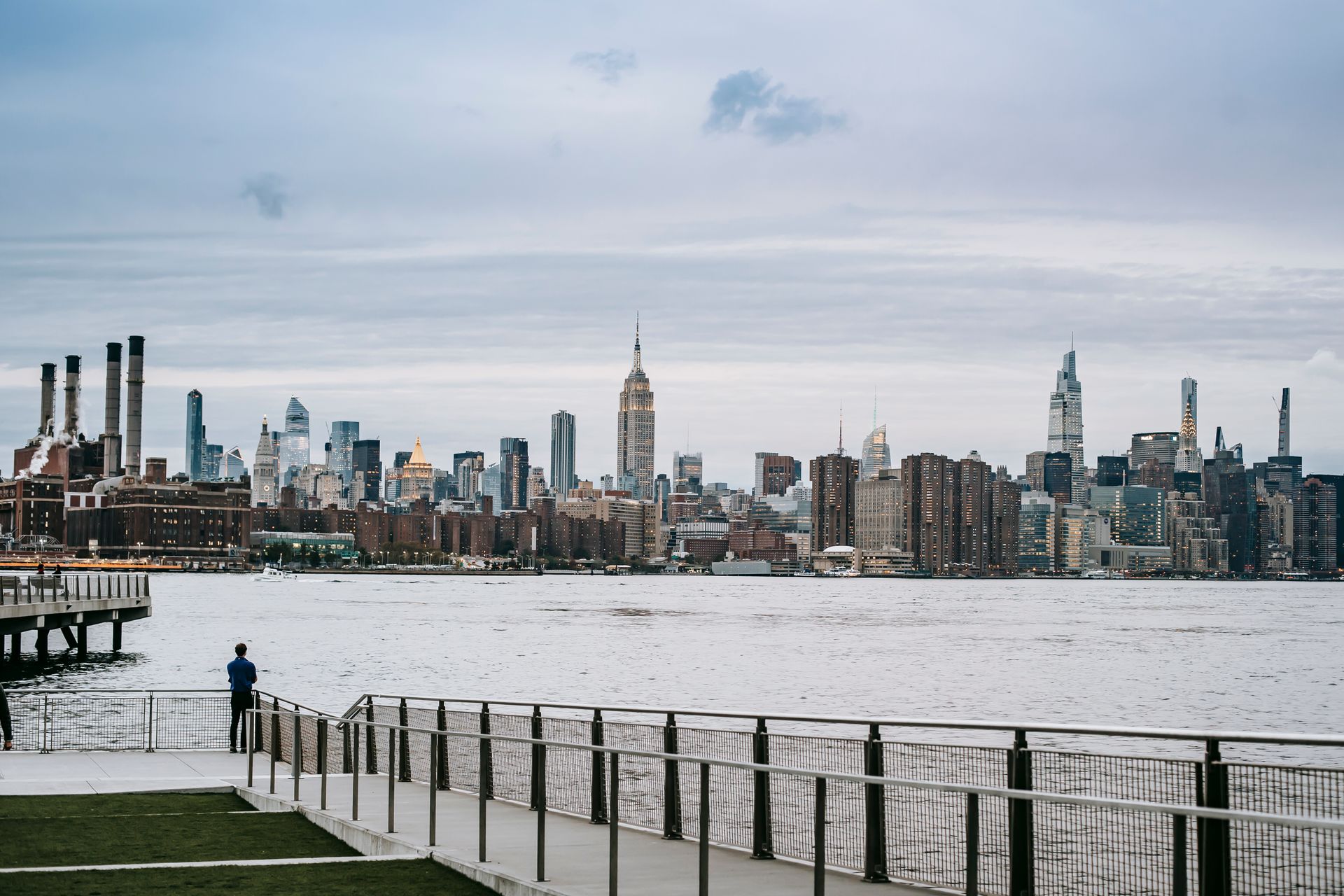 Man looking at Manhattan skyline from a pier across water.